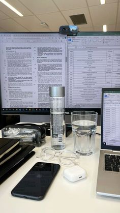 a laptop computer sitting on top of a desk next to a glass of water and a cell phone