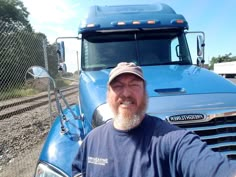 a man standing in front of a blue semi truck on the side of the road