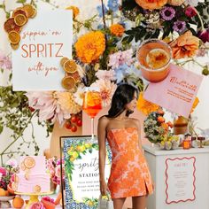 a woman in an orange dress standing next to a table with flowers and signs on it