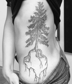 a woman's lower back with a tree and roots tattoo on her side ribcage