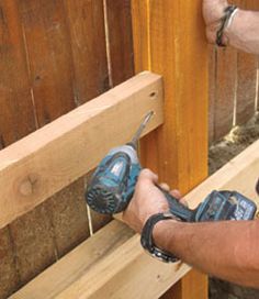 a man using a drill to fix a wooden fence