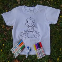 a t - shirt that has some markers and crayons next to it on the grass