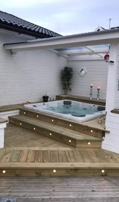 a hot tub sitting on top of a wooden deck next to a white building with lights