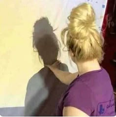 a woman standing in front of a white wall with her shadow on the wall behind her