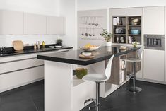 a modern kitchen with white cabinets and black counter tops, along with two bar stools