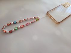 a cell phone is connected to a beaded necklace on a white surface with other beads