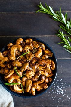 roasted cashews in a black bowl with rosemary sprigs on the side