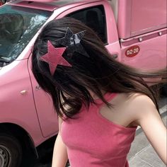 a woman with long black hair wearing a pink top and stars in her hair, standing next to a pink truck