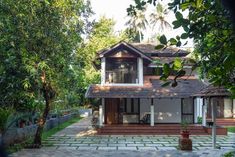 the house is surrounded by greenery and stone pavers, with trees in the background