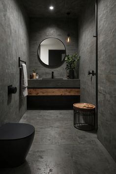 a modern bathroom with concrete walls and flooring is pictured in this image, there is a round mirror on the wall above the sink