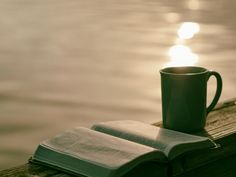 an open book and coffee cup sitting on a dock next to the water at sunset