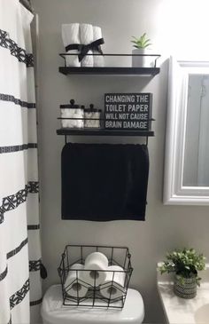 a white toilet sitting next to a sink under a window in a bathroom with black and white decor