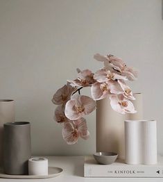 three vases with flowers in them on top of a white shelf next to a book