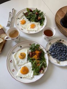 two plates with eggs and blueberries on them next to toast, buttered bread and coffee