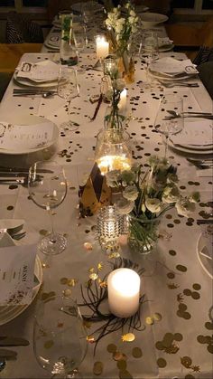 the table is set with white and gold plates, silverware, candles, and confetti