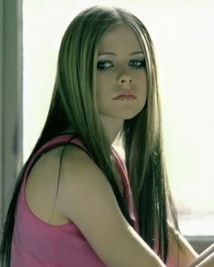 a woman with long hair and blue eyes sitting in front of a window looking at the camera