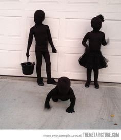 three children dressed up in black standing next to a garage door and holding buckets