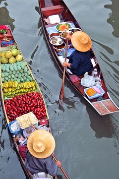 two boats with people in them floating on the water near other boats filled with food