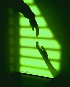 two hands reaching towards each other in front of a green light