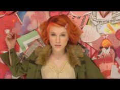 a woman with red hair standing in front of a wall full of paper heart shapes