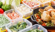 several plastic containers filled with food on top of a wooden table next to vegetables and meat