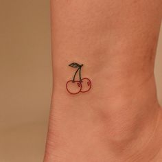 a small cherry tattoo on the side of a woman's ankle, with two cherries attached to it