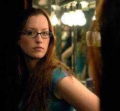 a woman with glasses standing in front of a mirror