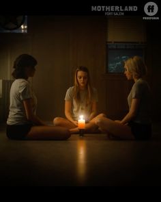 three women sitting on the floor in front of a candle