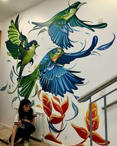 a woman sitting on the floor in front of a wall with birds painted on it