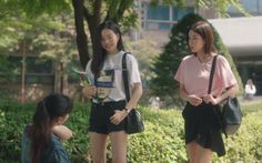 two young women standing next to each other in front of trees and bushes, one holding a cell phone