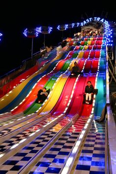 several people are riding down an indoor slide at night time with colorful lights on them