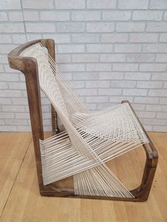 a chair made out of rope sitting on top of a wooden floor next to a brick wall