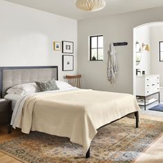 a bedroom with a bed, dresser and rug on the hardwood floor in front of it