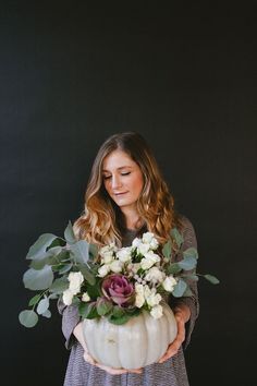 a woman holding a white pumpkin filled with flowers