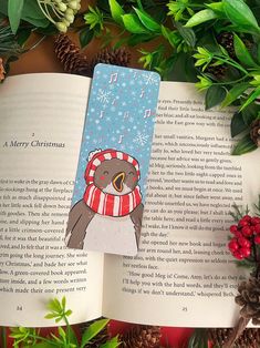 an open book with a bear wearing a scarf on it and christmas decorations around it