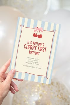 a person holding up a birthday card with cherries on the front and bottom, it's adeline's cherry first birthday