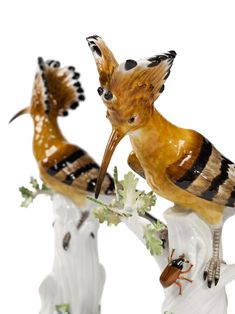 two figurines of birds perched on top of each other, one with an insect in it's mouth