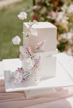 a three tiered white cake with flowers on the top and bottom is sitting on a table