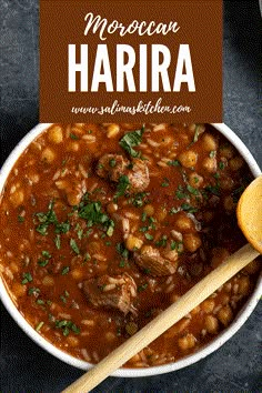 a white bowl filled with beans and meat next to a wooden spoon on top of a table