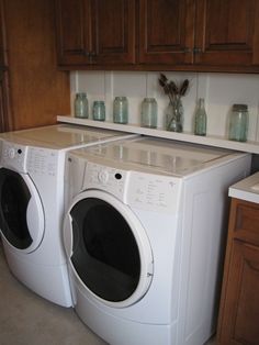 a washer and dryer in a kitchen next to wooden cupboards with vases on the counter