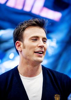 a man with his eyes closed standing in front of a blue background and smiling at the camera