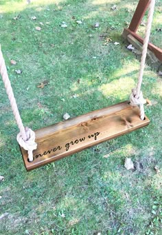 a wooden sign that says never grow up hanging on a rope swing in the grass