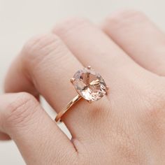 a woman's hand holding a ring with an oval shaped morganite stone on it