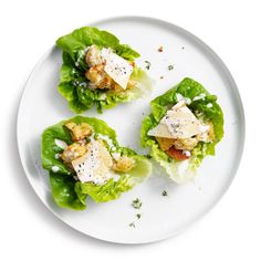 three lettuce leaves with cheese and other toppings on a white plate against a white background