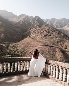 a woman standing on top of a balcony next to mountains