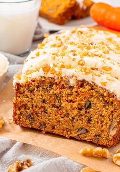 carrot cake with white frosting and nuts on a cutting board next to other food