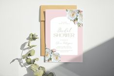 a pink and white floral bridal shower card on top of a wooden frame next to a plant