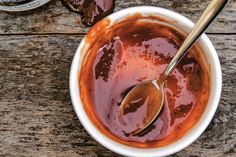 a spoon in a bowl filled with sauce on top of a wooden table next to two bottles