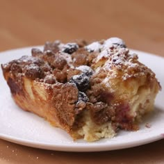 a white plate topped with a piece of cake covered in powdered sugar on top of a wooden table