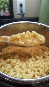 a ladle full of macaroni and cheese being stirred with a wooden spoon